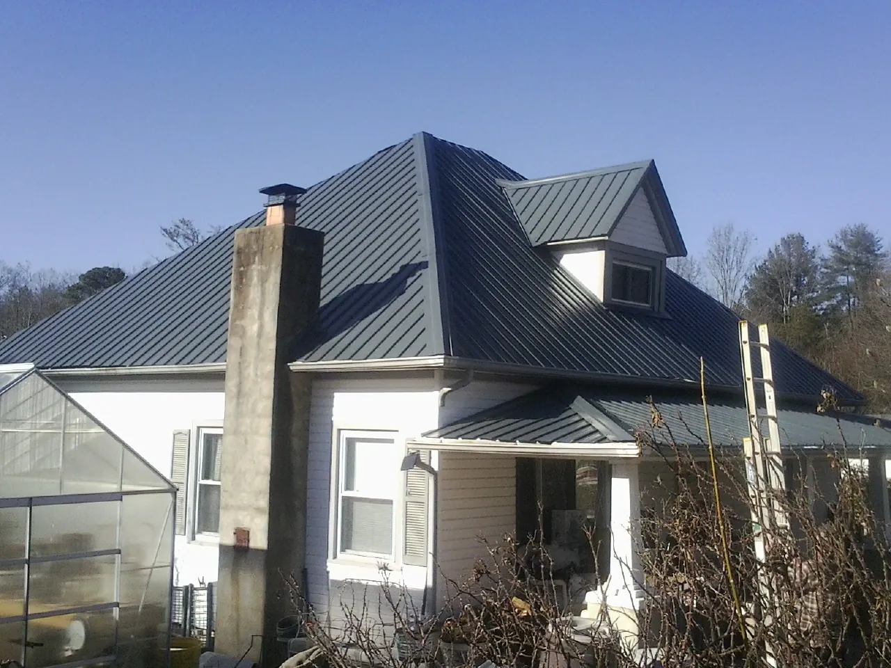 Dark blue standing seam metal roof on a white farmhouse with dormer — Slate & Tile Roof Repair by Roofing Brothers in Asher