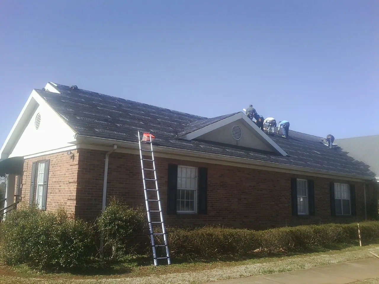 Crew tearing shingles off a brick ranch roof with a ladder set — Metal Roof Repair work by our crew in Asher