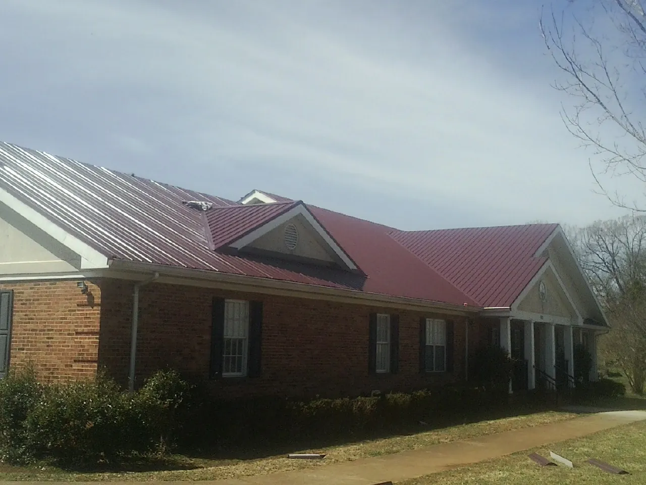 Red metal roof with gabled entries on a long brick building, from a Hail Damage Roof Repair job in Asher