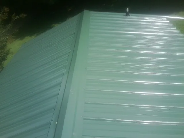 New green metal panels meeting at the ridge of a roof — Flat Roof Repair work by our crew in Asher