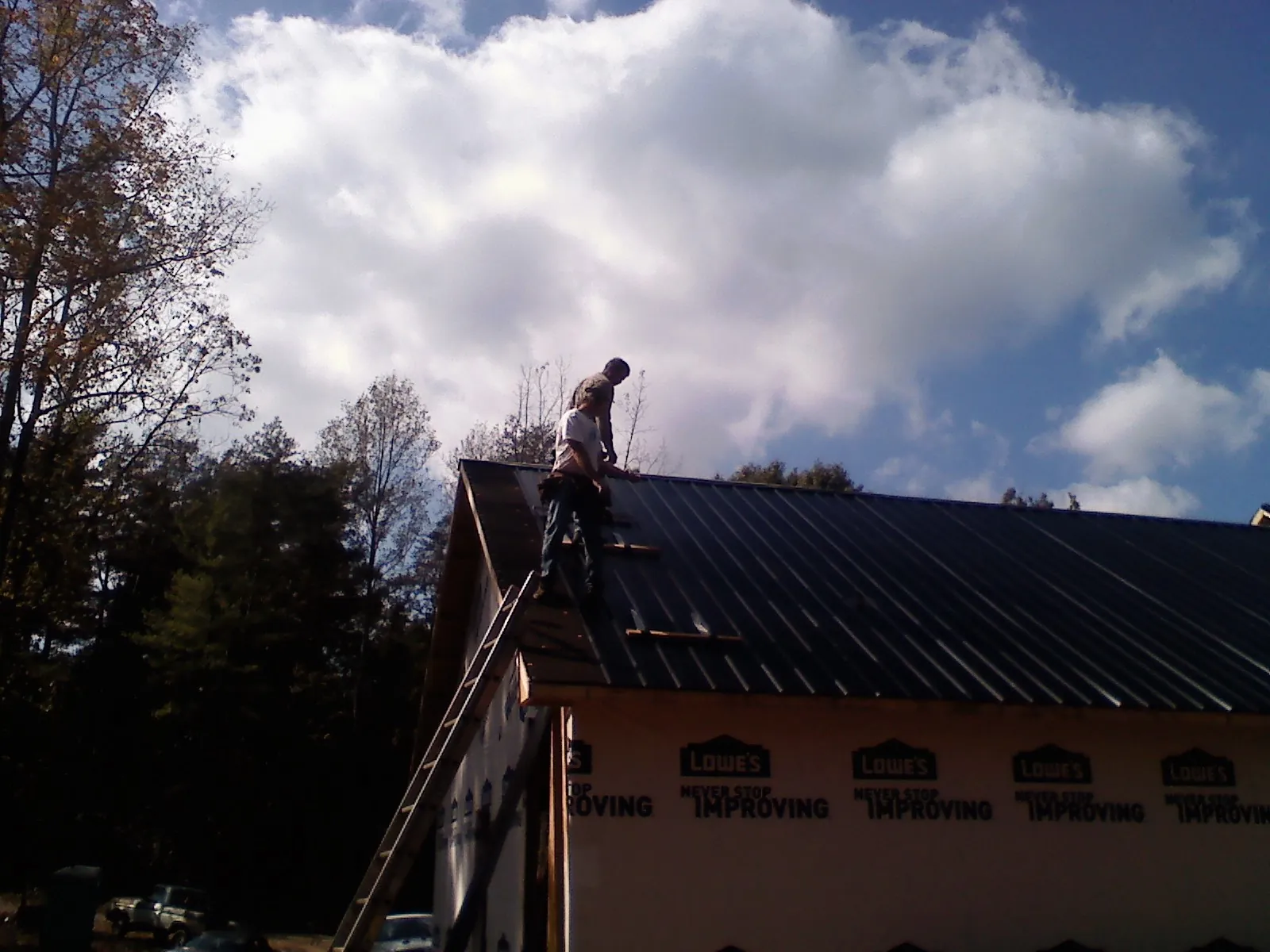 Roofer fastening dark metal panels high against a cloudy sky, from a Roof Inspection job in Asher