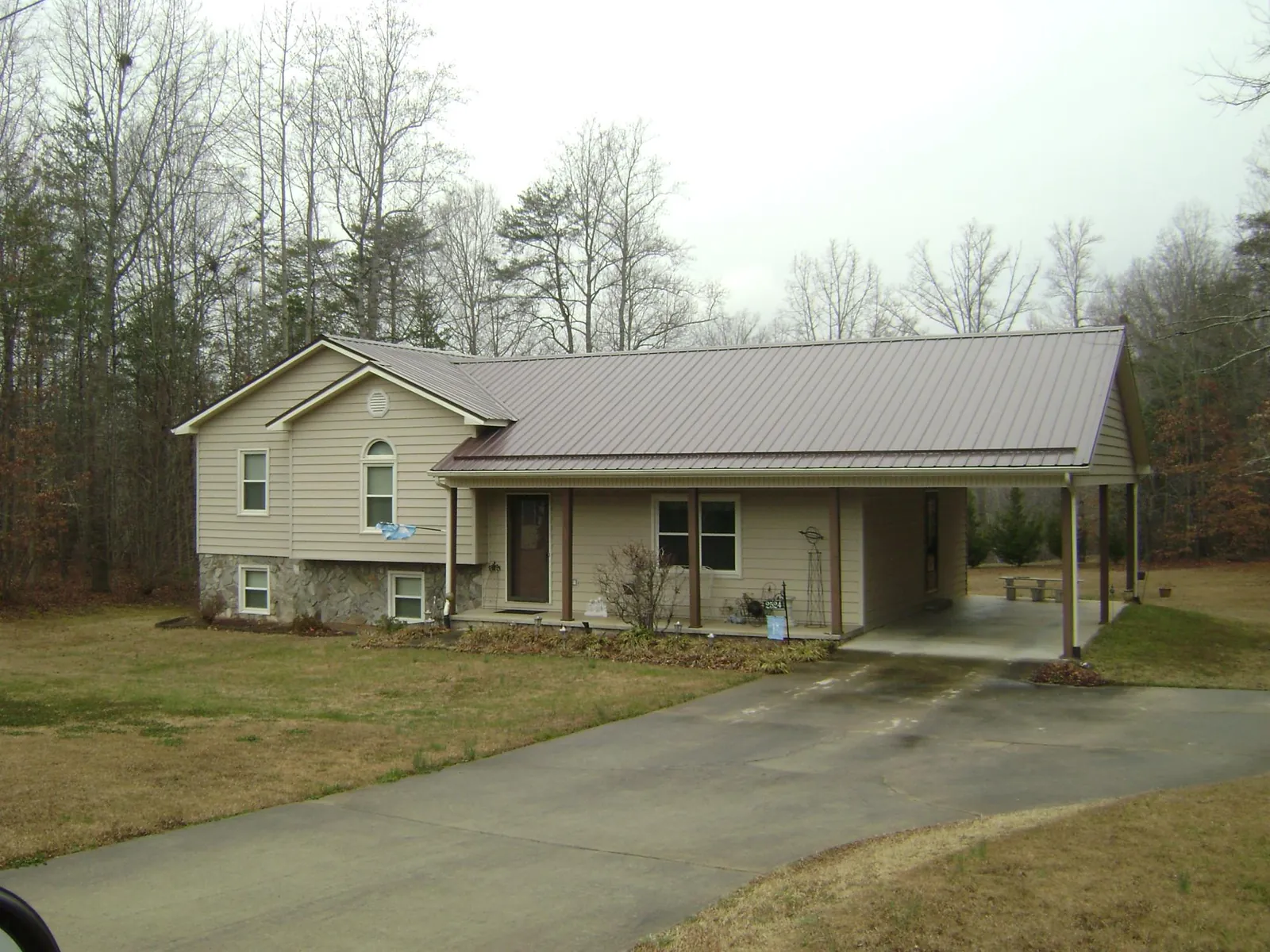 Brown metal roof on a tan split level home with an attached carport in Asher